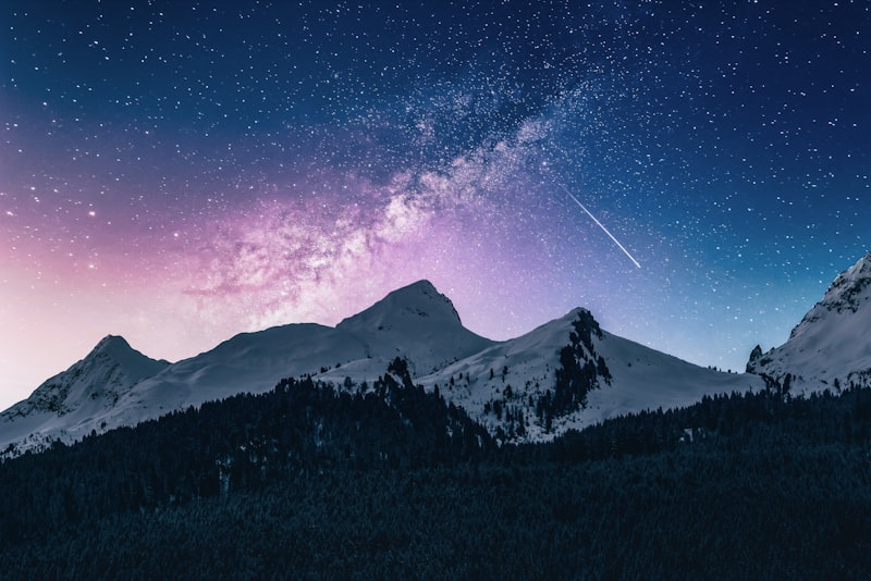Snow-capped mountain peaks and pine forest beneath a starry night sky with the Milky Way and a shooting star